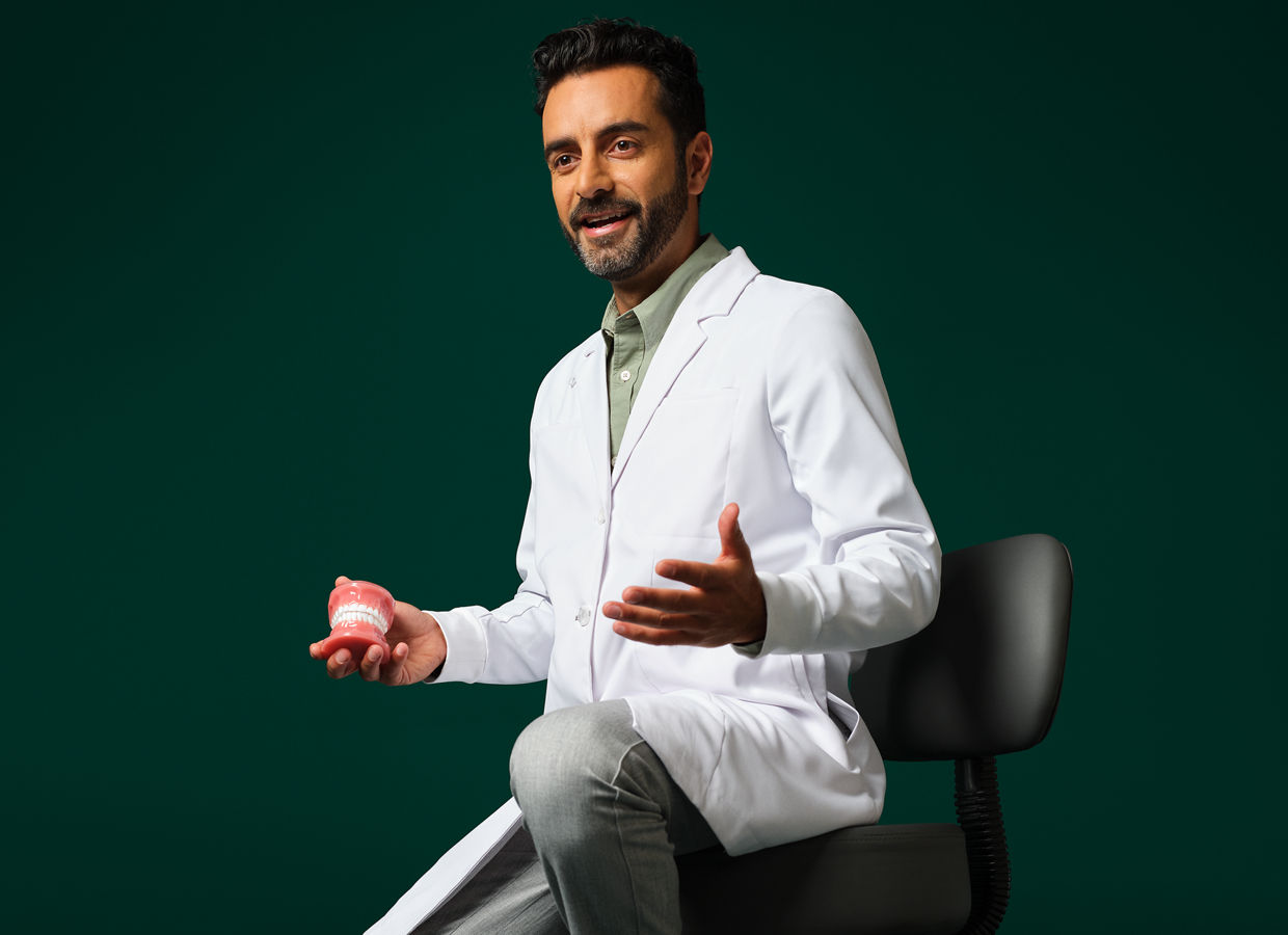 Male orthodontist wearing a white coat sitting holding a typodent