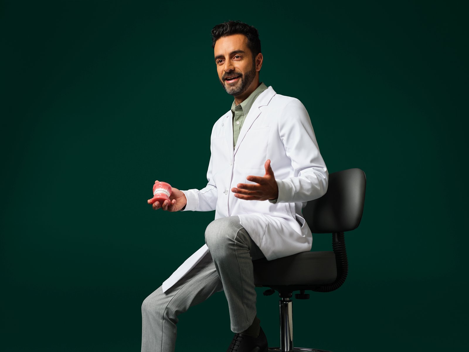 Orthodontist die een witte jas draagt zit en houdt een typodont vast.
