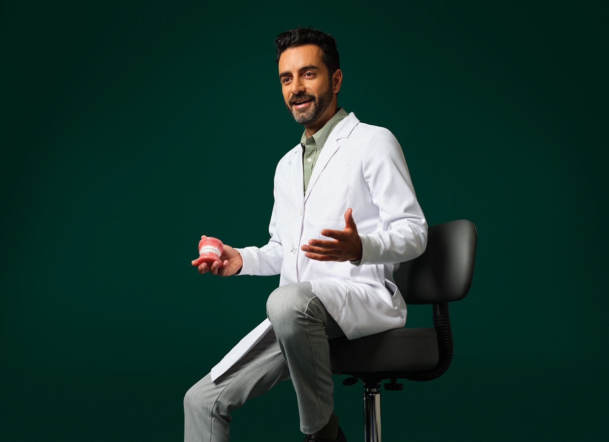 Male orthodontist wearing a white coat sitting holding a typodent