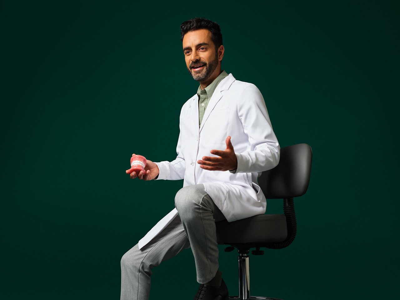 Orthodontist wearing a white coat sitting holding a typodont.