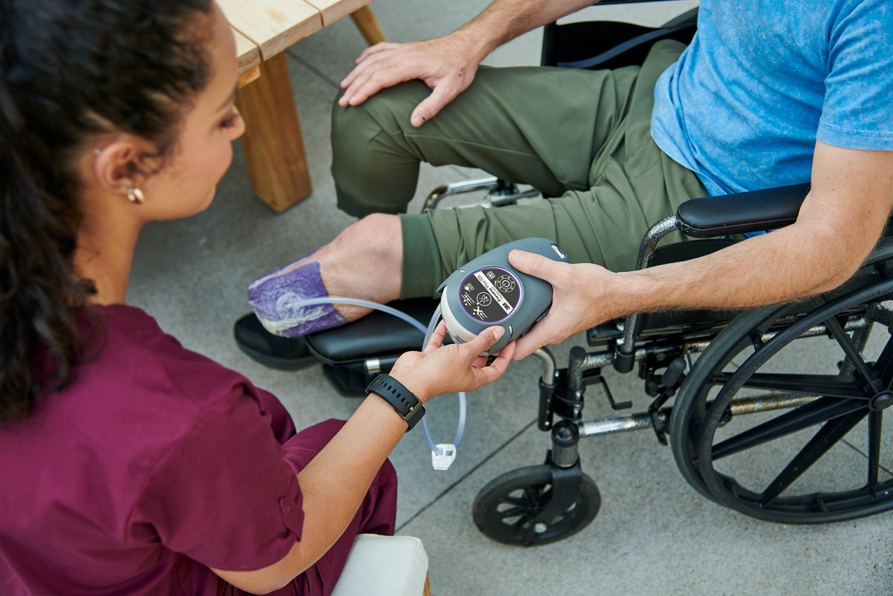 Man sitting in wheelchair with amputated legs wearing 3M™ Prevena Restor™ Adapti•Form™ Dressing and 3M™ Prevena™ Plus 125 Therapy Unit talking with home care nurse on patio. Lifestyle image, people image, product application image, high res, 300dpi, rgb, tiff