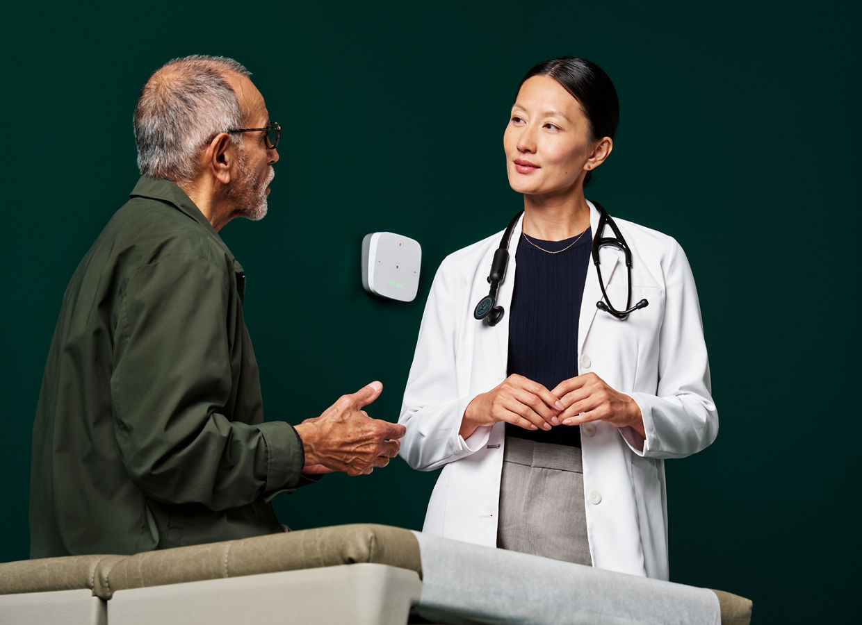 Portrait of a male patient interacting with a female primary care doctor in an exam room on a dark green background on a dark green background.