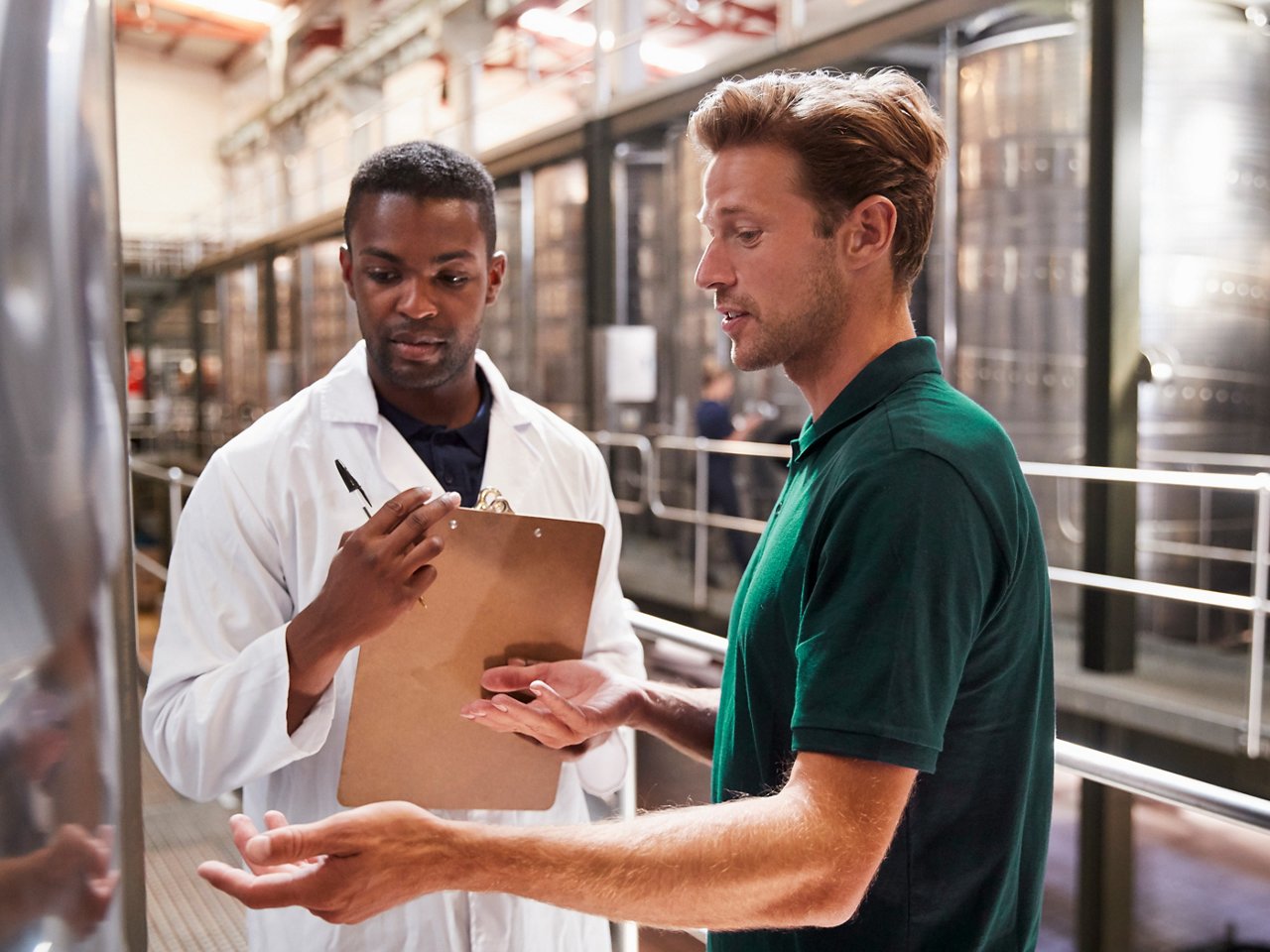 Two men talk and inspect vats in a modern winemaking factory