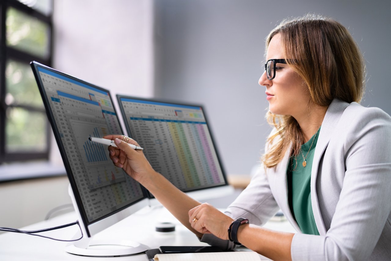 Female employee seated at her desk viewing information on one of two monitors.