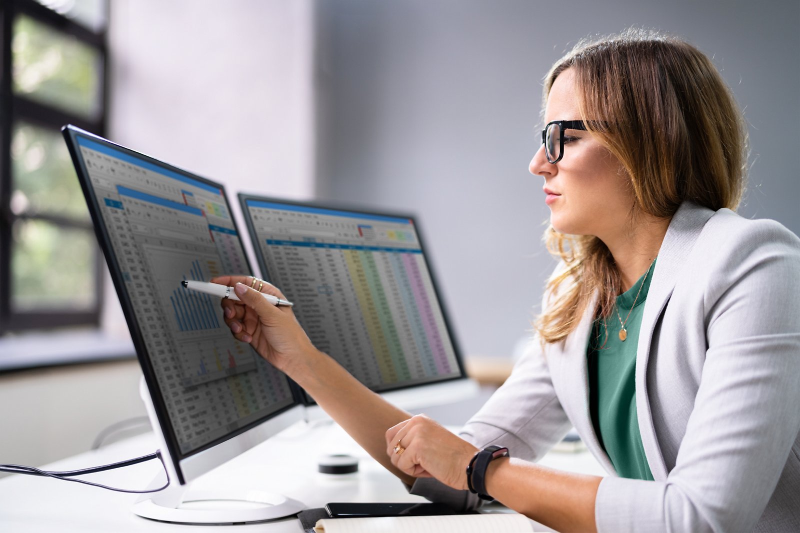 Female employee seated at her desk viewing information on one of two monitors.