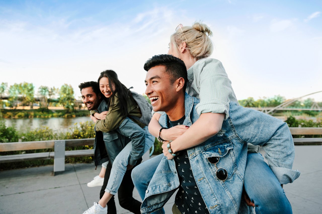 Playful young couples piggybacking along waterfront.