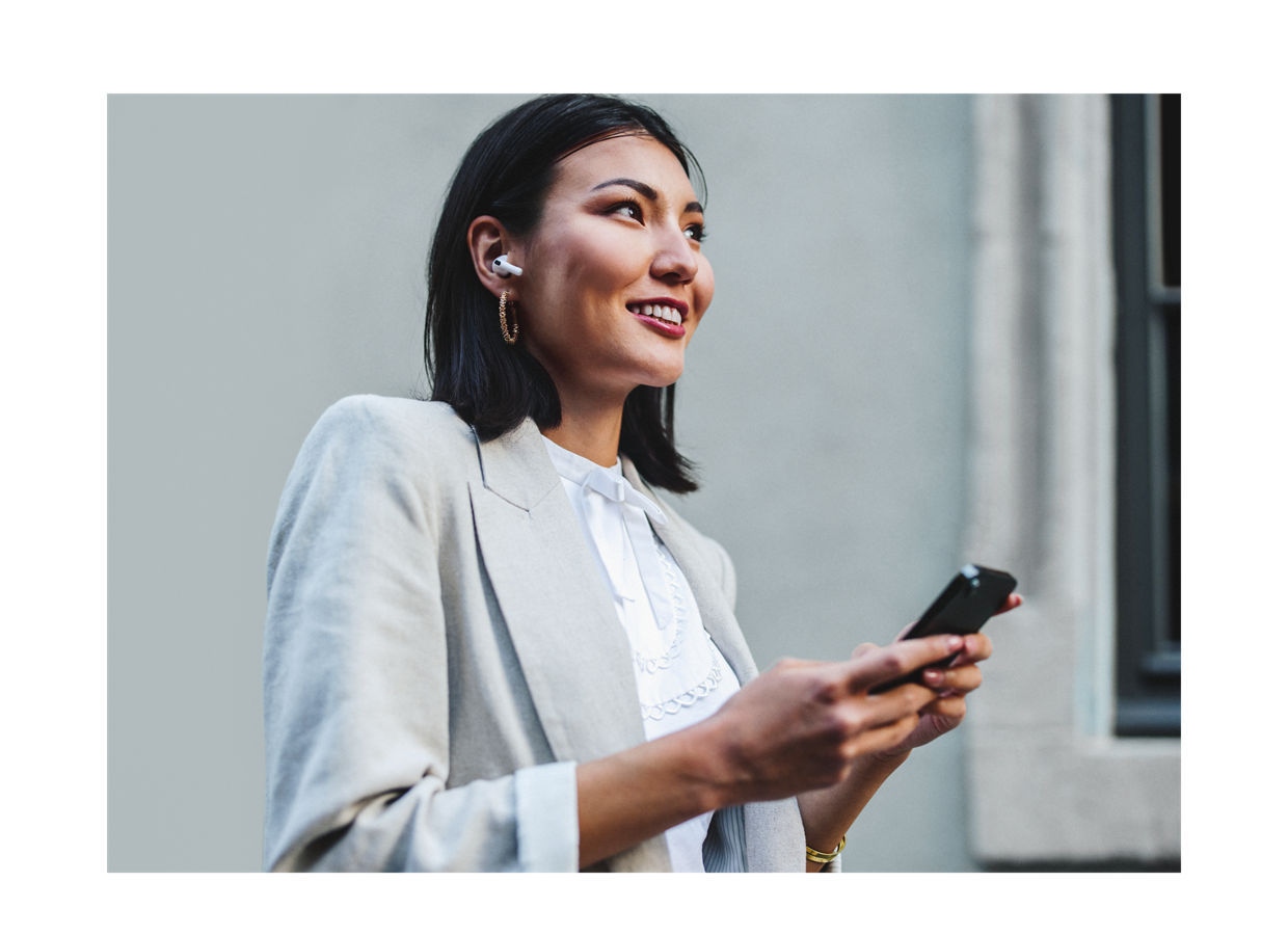 Smiling, young professional business woman interacting with her cell phone and wearing earbuds.