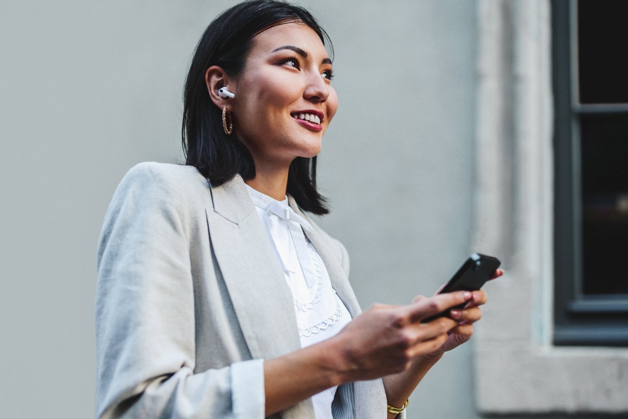 Woman using a smartphone while walking around the city in the morning. Happy business woman listening to music with earphones. This photo has intentional use of 35mm film grain.; Shutterstock ID 2258543093; purchase_order: credit card; job: Brand Design - Mark Bonesteel; client: mwbonesteel1@mmm.com; other: USA