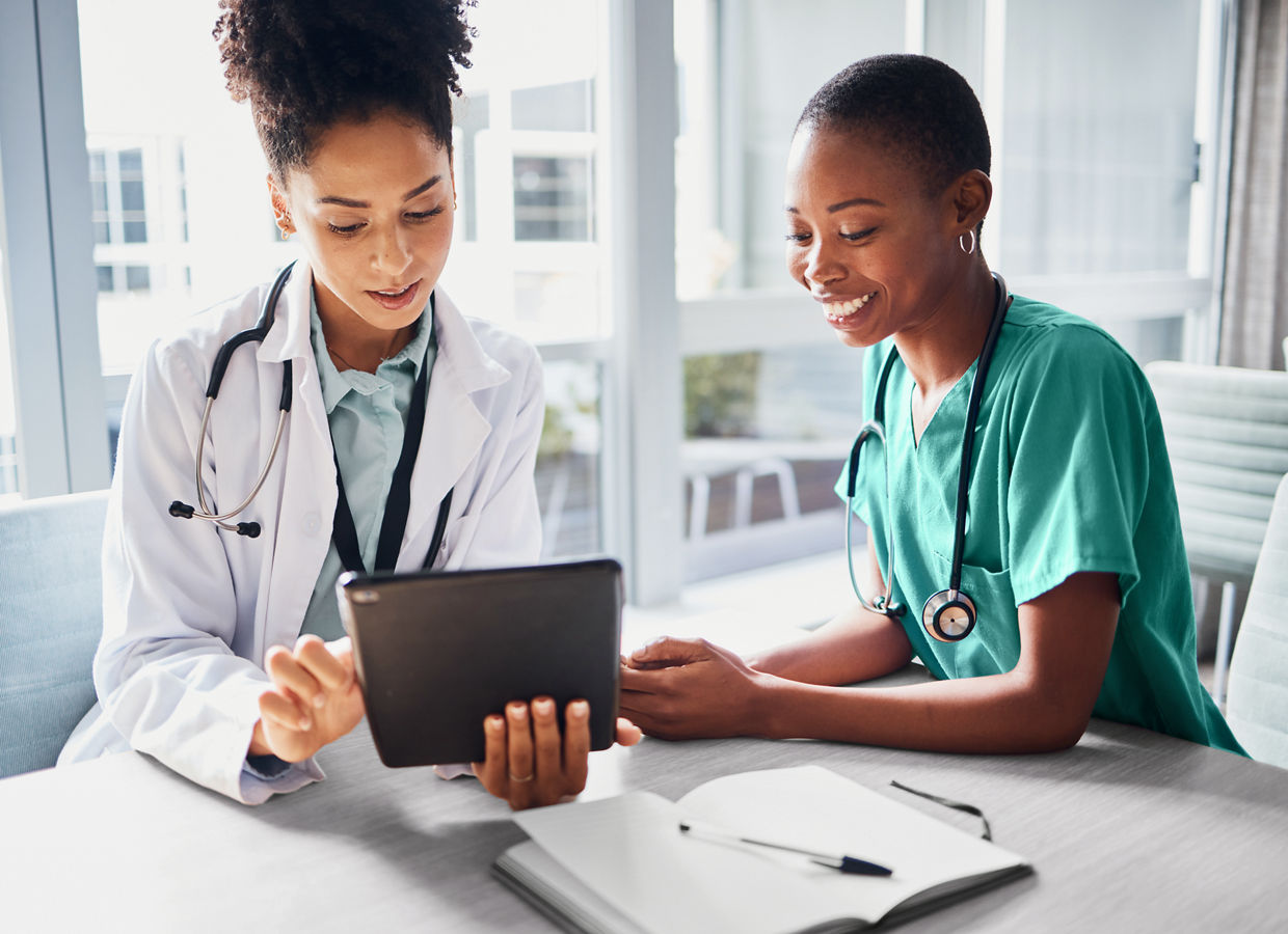 A nurse and a doctor, review results together on a tablet in a healthcare setting.