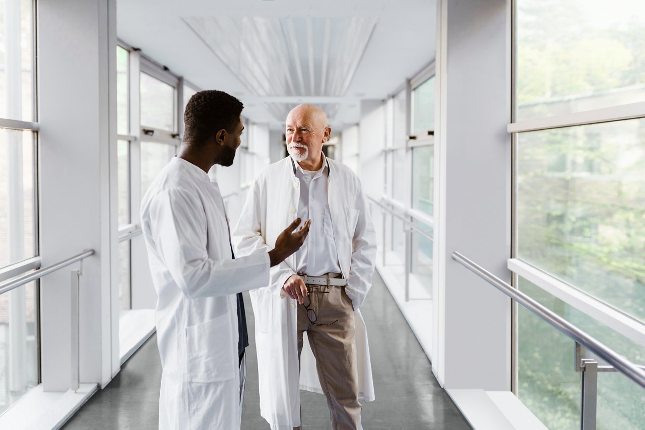 A male doctor and physician nurse discussing while standing in corridor at hospital.