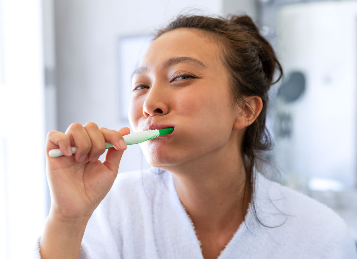 A woman brushing her teeth while looking in the mirror.