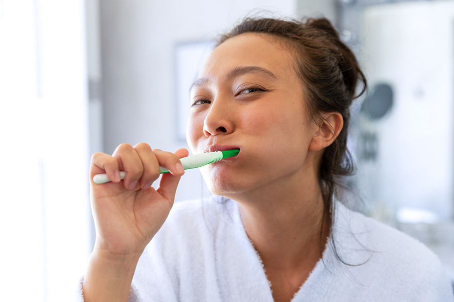 Happy asian woman wearing bathrobe looking in bathroom mirror brushing teeth. lifestyle, self care, health and beauty.