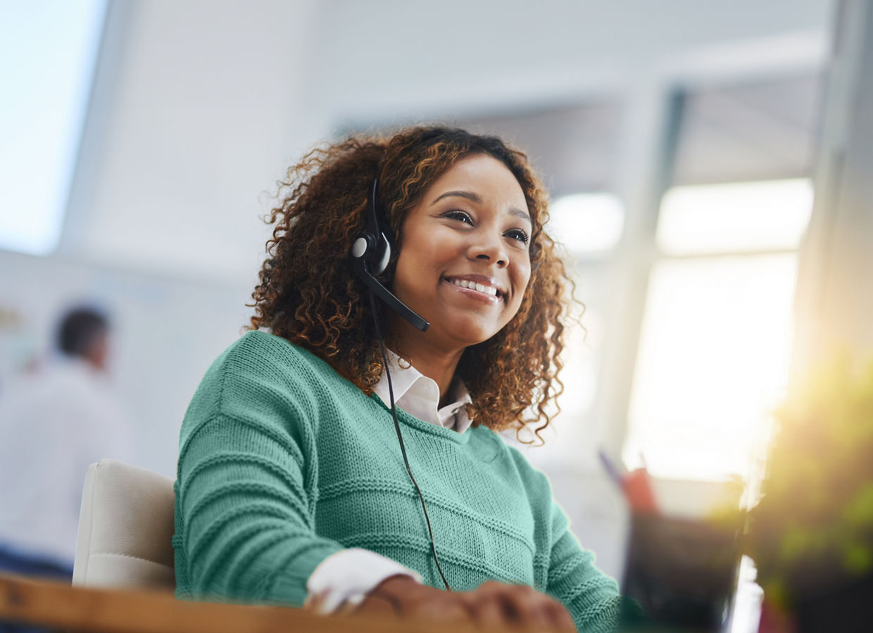 Image of a female call center employee working at a desk, wearing a green sweater.