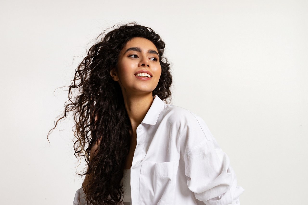 Portrait waist up of a woman smiling looking to the side on a white background.