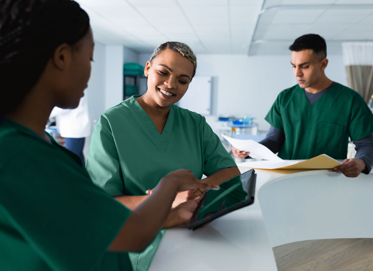 Tres médicos discutiendo sobre el trabajo, usando una tableta en el mostrador de recepción del hospital.