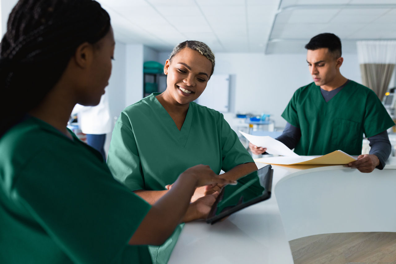 Tres médicos discutiendo sobre el trabajo, usando una tableta en el mostrador de recepción del hospital.