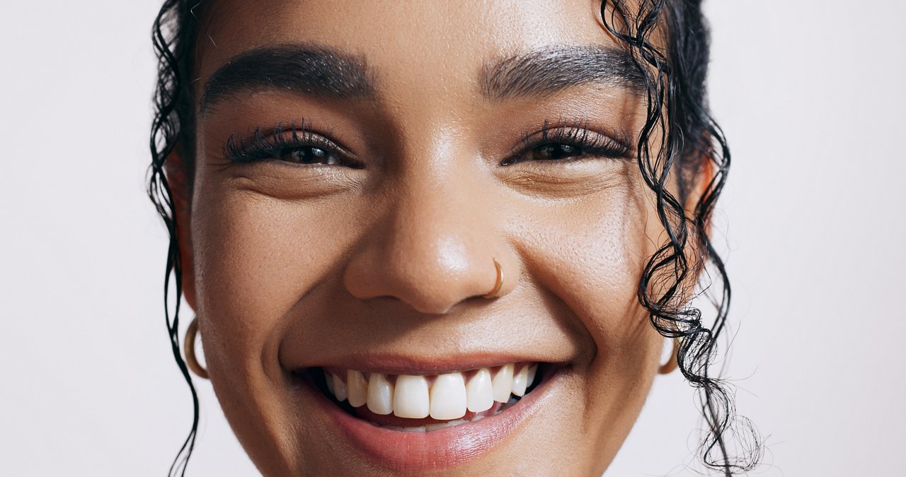 Closeup portrait of a woman smiling directly at the camera on a white background.