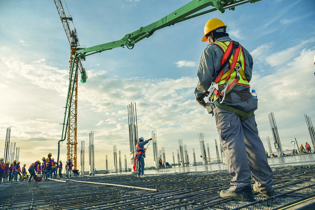 A construction worker control a pouring concrete pump on construction site and sunset background