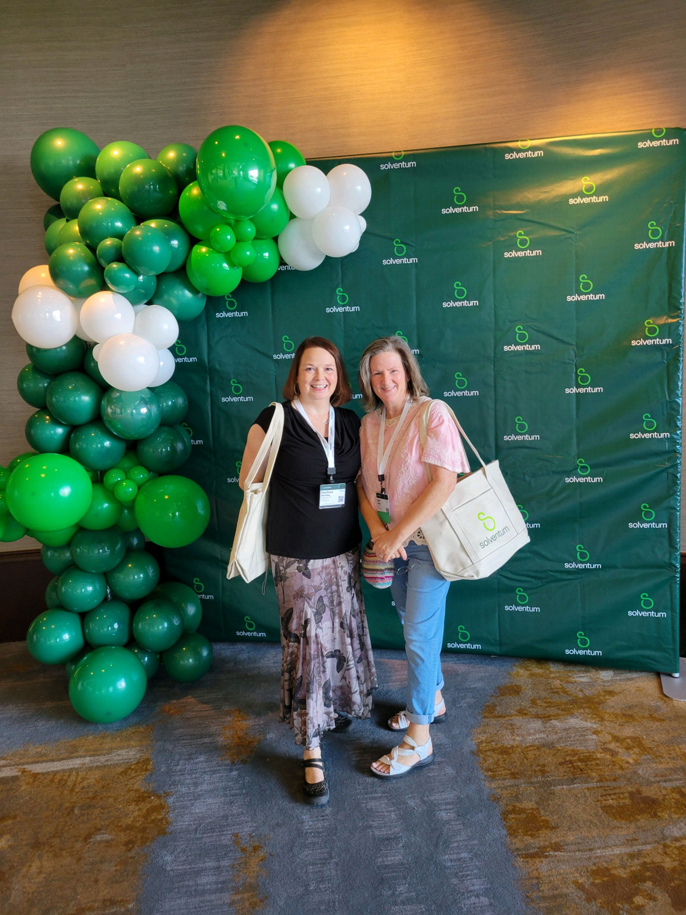Two women at the 2024 Solventum Summit Awards standing in front of a green background with balloons and smiling.