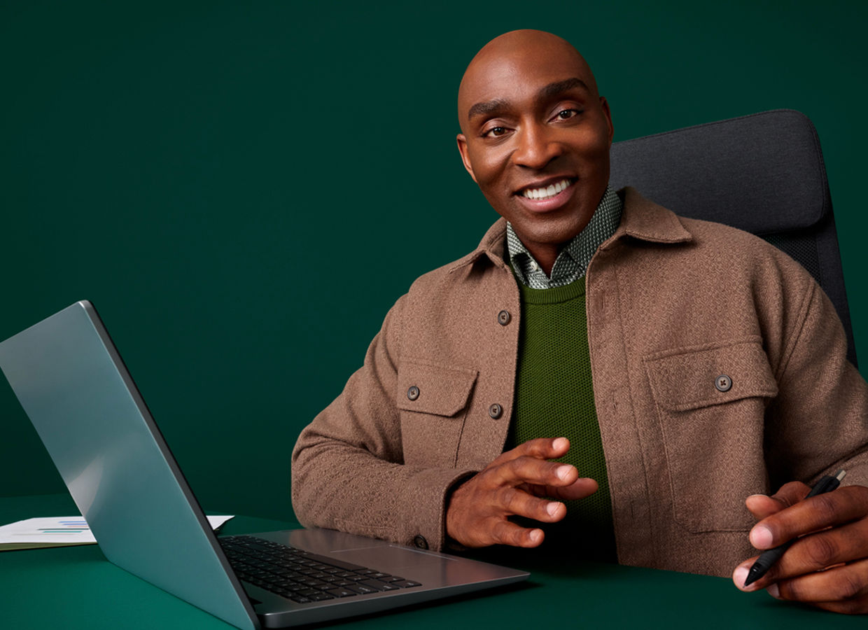 Portrait of a male health administrator at his desk on a dark green background.