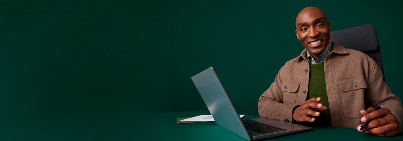 Portrait of a male health administrator at his desk on a dark green background.