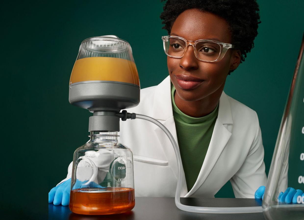 Portrait of a female process development scientist in a lab with Harvest RC Chromatographic Clarifier BT500 equipment on a dark green background.