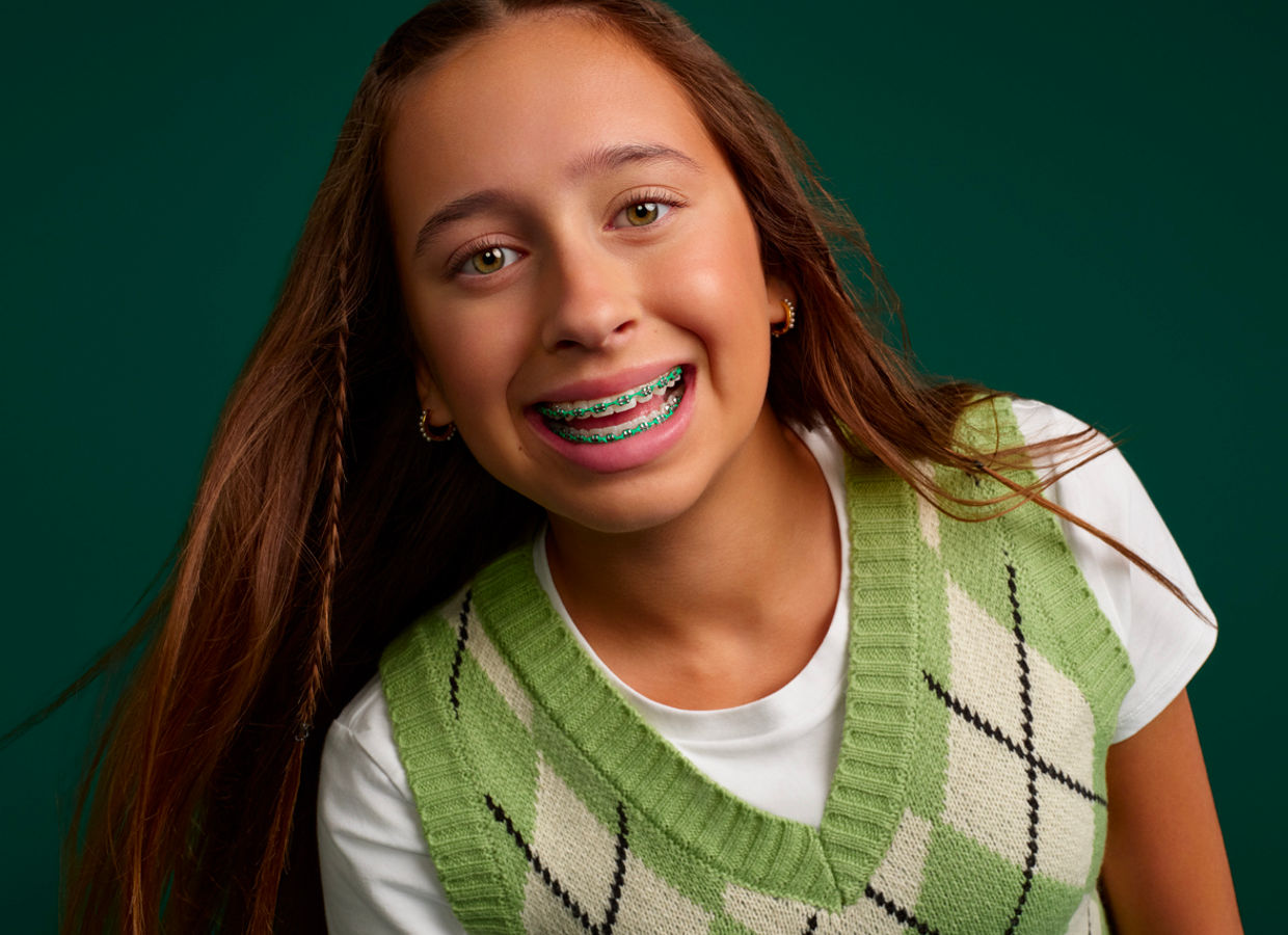 Portrait of a young girl smiling with braces on a dark green background.