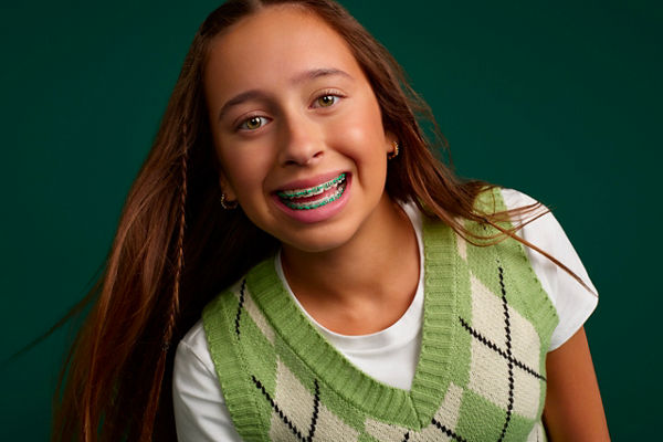 Portrait of a young girl smiling with braces on a dark green background.