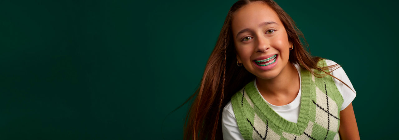 Portrait of a young girl smiling with braces on a dark green background.