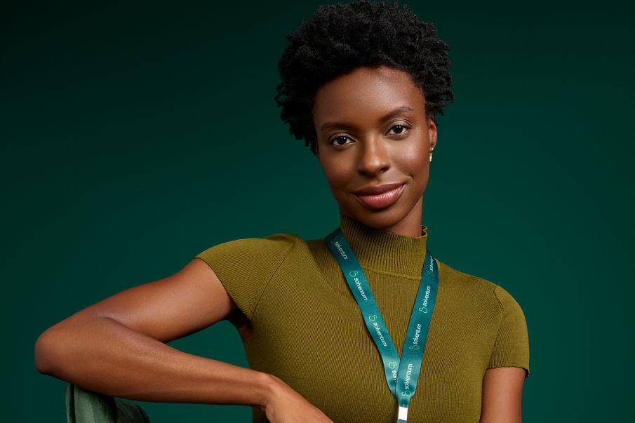 Portrait of a Solventum female office worker seated in a chair on a dark green background.