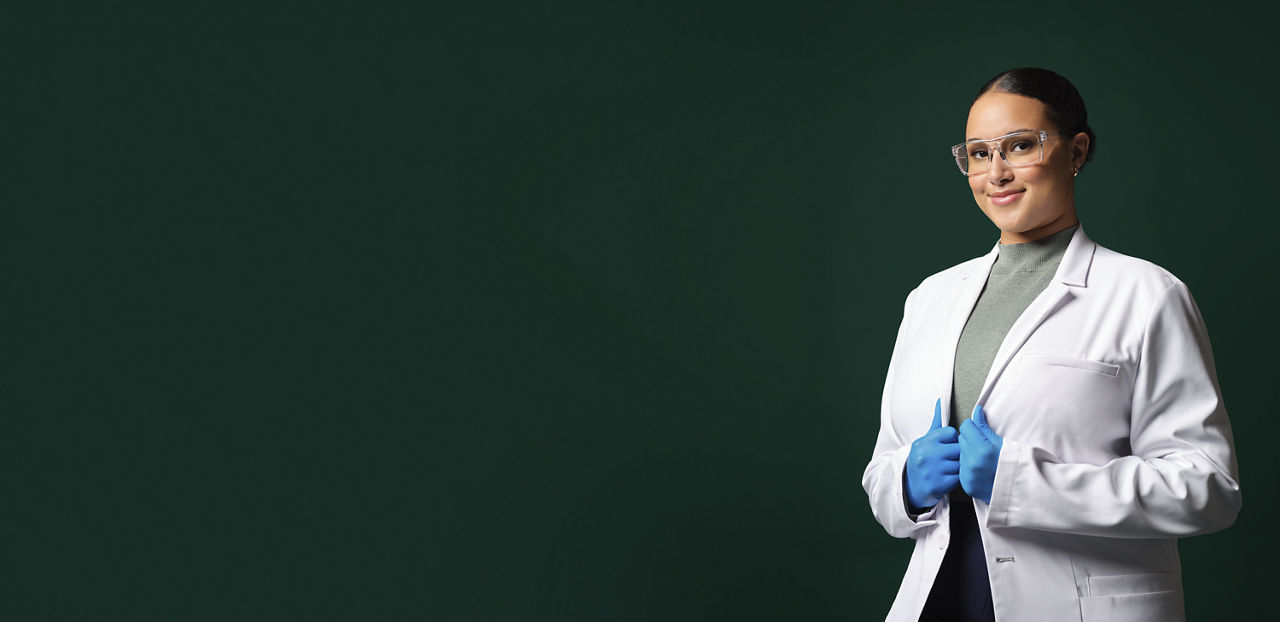 Anwendungstechnikerin trägt weißen Laborkittel, Schutzbrille und blaue Handschuhe