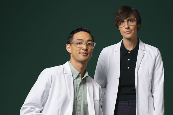 Two male engineers/scientists in white coats and blue gloves by a small table with lab equipment on it