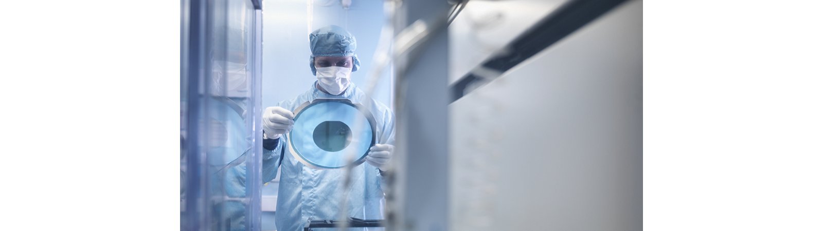 Electronics worker holding silicon wafer by cutting machine in clean room