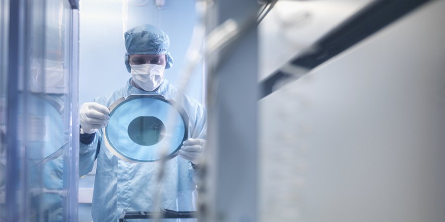 Electronics worker holding silicon wafer by cutting machine in clean room