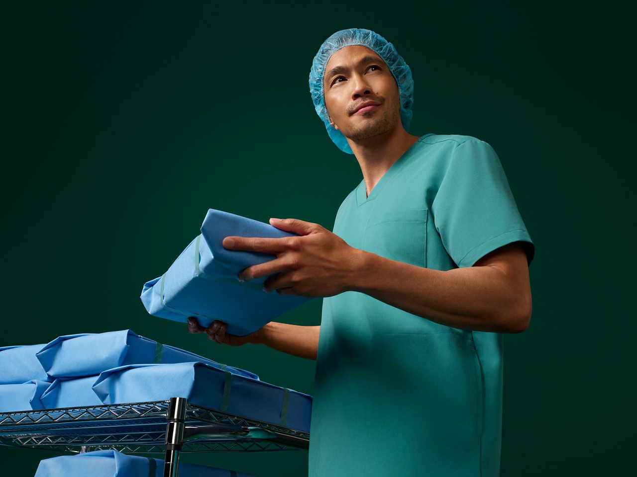 Portrait of a sterilization processing technician stocking inventory on a dark green background.