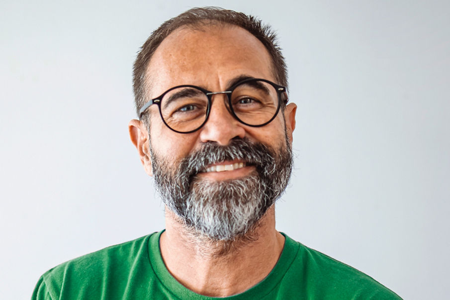 An image of a man in a green shirt with glasses smiling at the camera