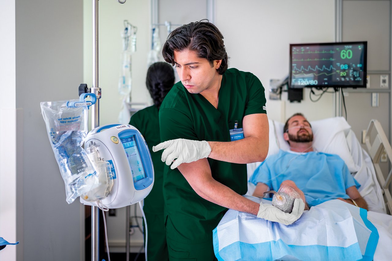 Nurse adjusting VAC Therapy treatment for patient lying in bed with amputated leg while another nurse checks IV bag.