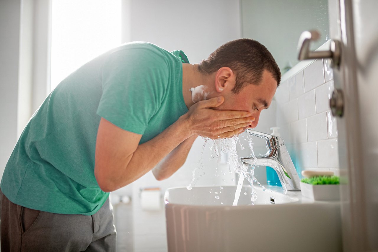 Mixed race mid adult man is cleansing his face after shaving at the sink in the bathroom in the morning