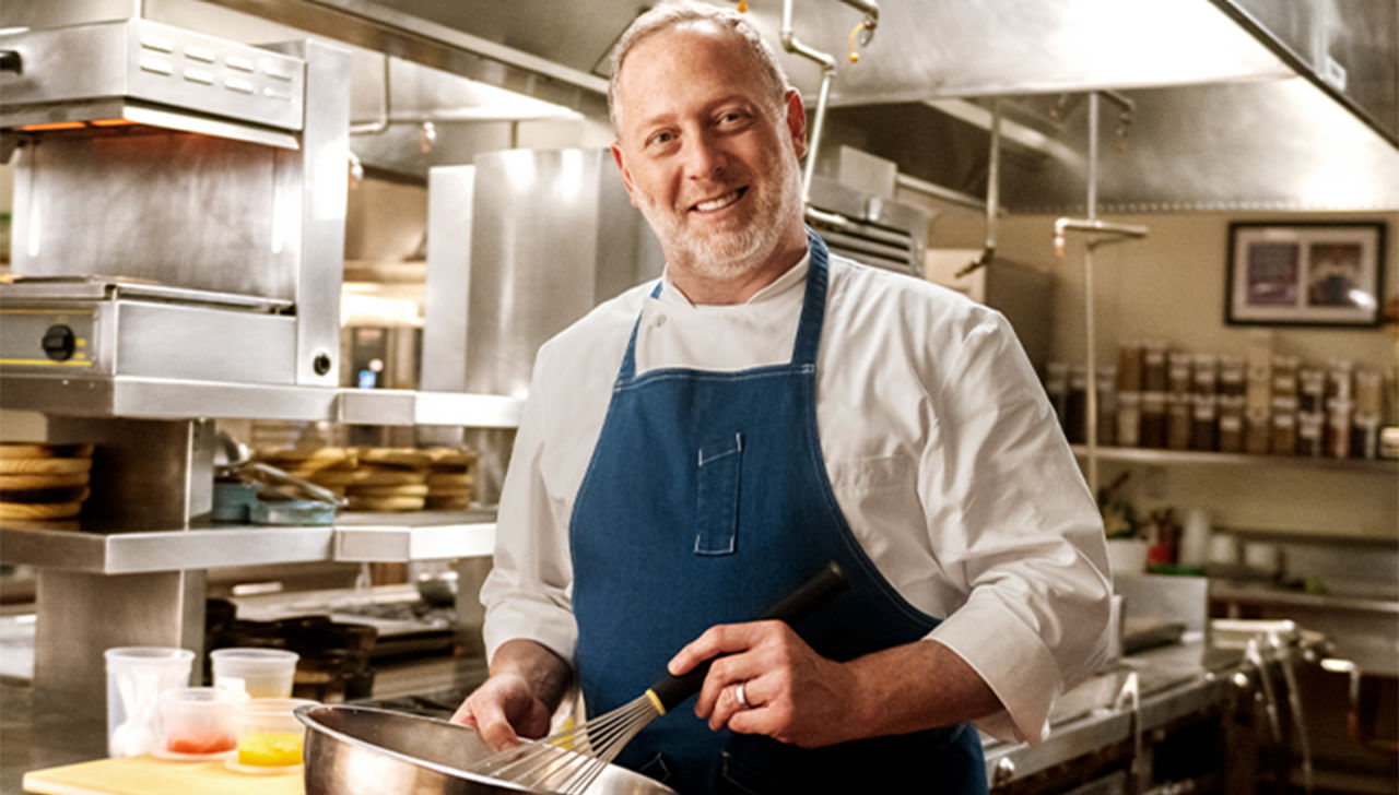 Franklin Becker standing in kitchen holding a bowl and whisk