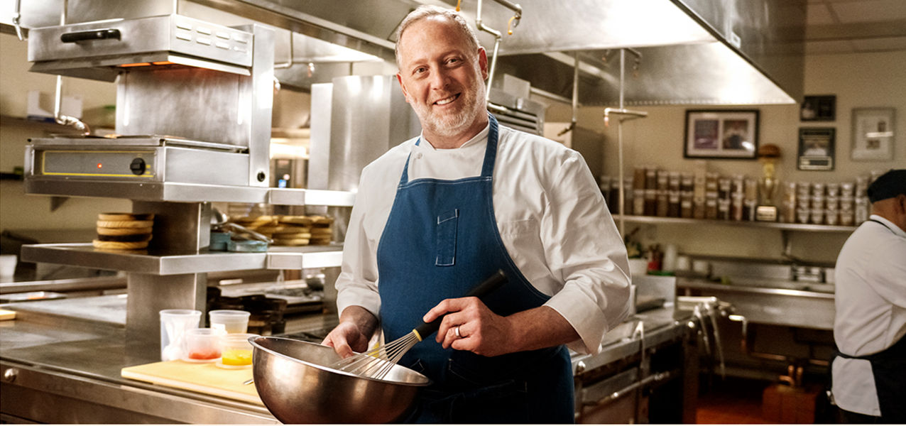 Franklin Becker standing in kitchen holding a bowl and whisk