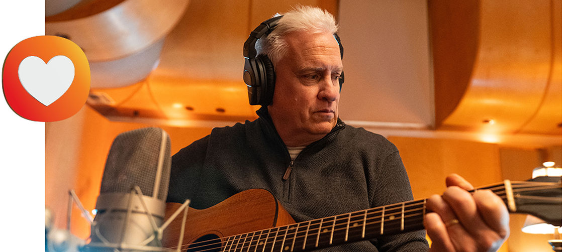 Tom strumming a guitar with a heart icon to the left