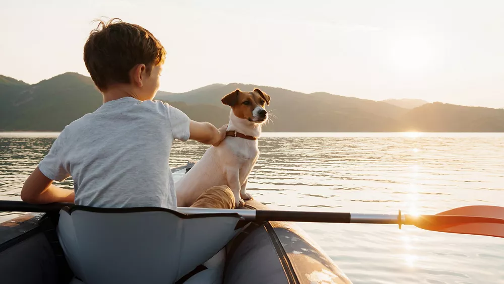 Happy boy with his dog Jack Russell Terrier paddling an inflatable kayak on the water mountain lake