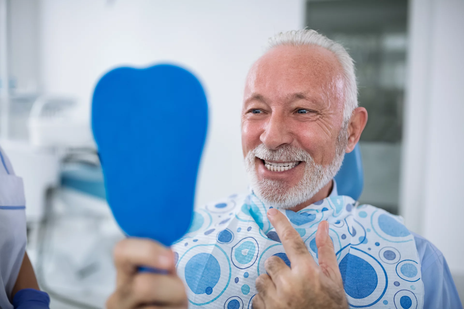 Smiling and satisfied patient after treatment looks at teeth in mirror