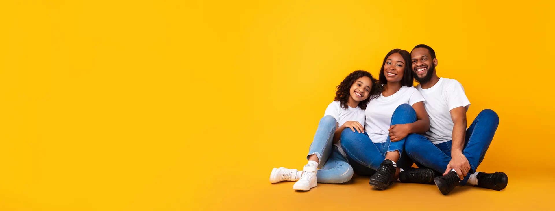 Happy Loving Family. African American man, woman and girl sitting on the floor isolated on yellow studio wall. Smiling husband and wife posing with daughter at camera, banner, panorama, copy space