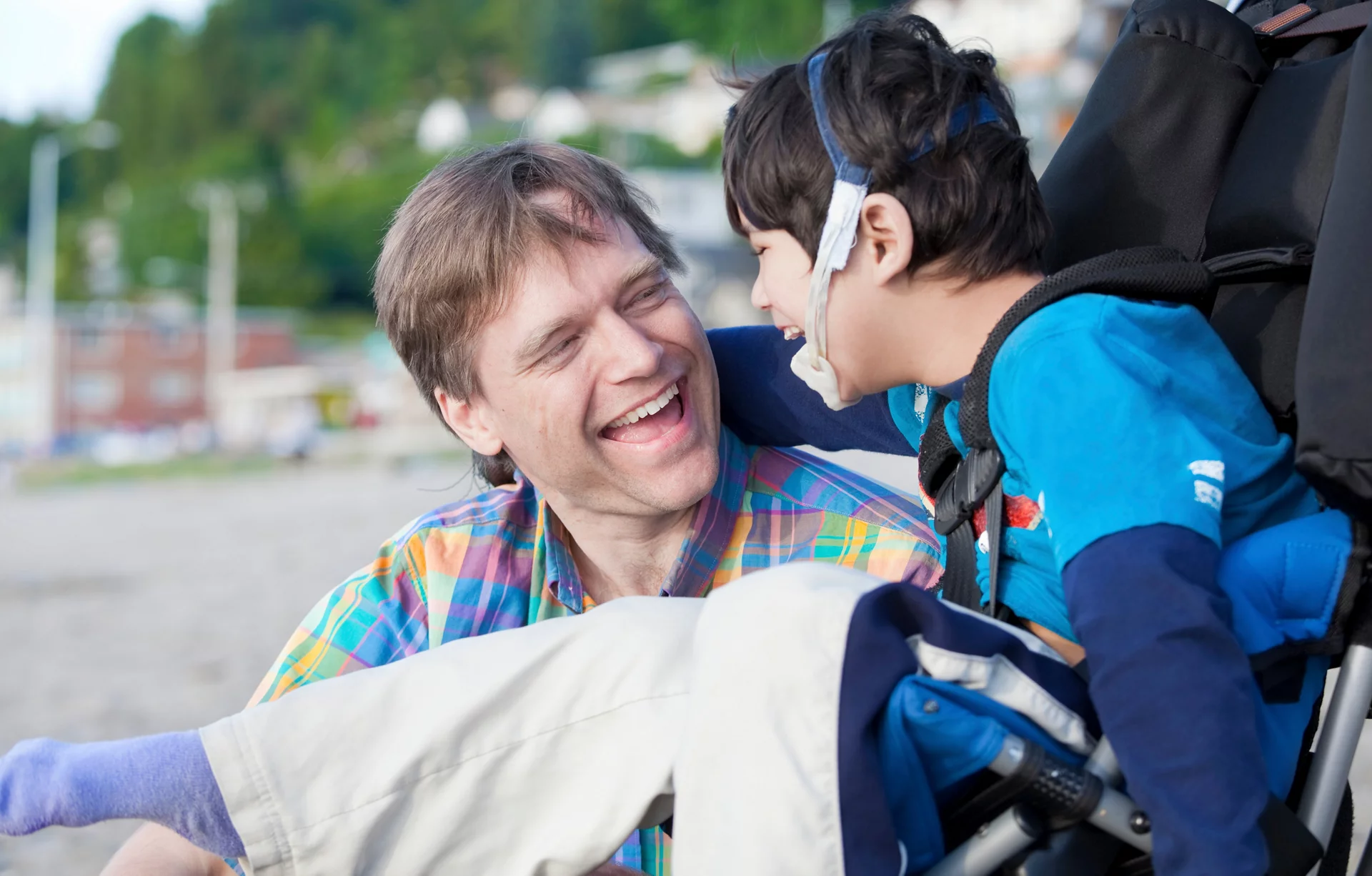 Father and disabled five year old son laughing together on beach