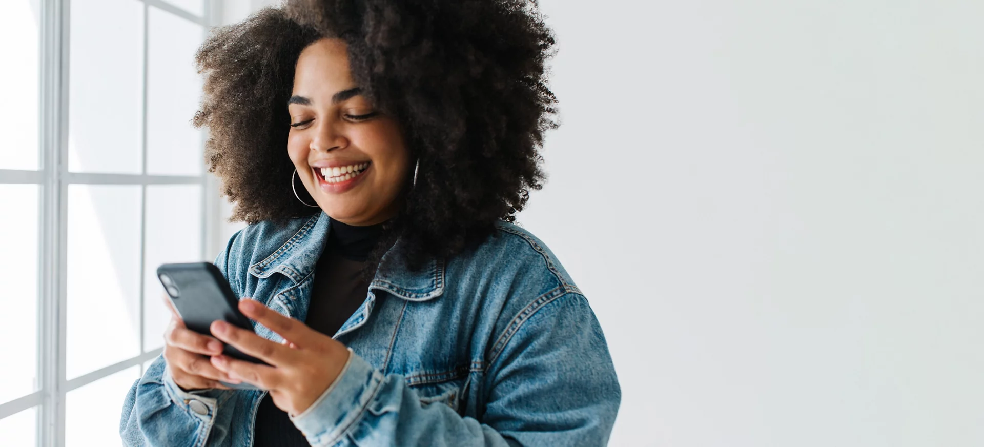 Smiling woman using her mobile phone. Female wearing denim jacket reading text message on smart phone.