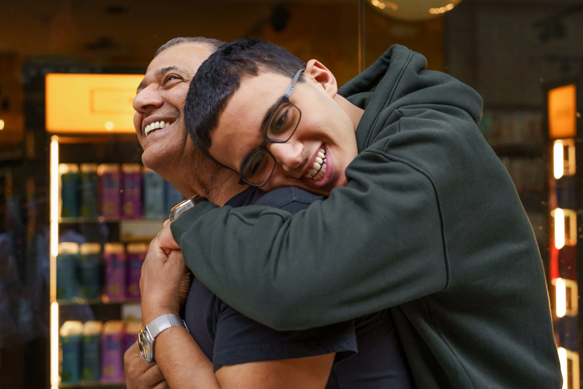 Hug for dad. A teen boy leans over to hug his father, who to be smiling at him.
