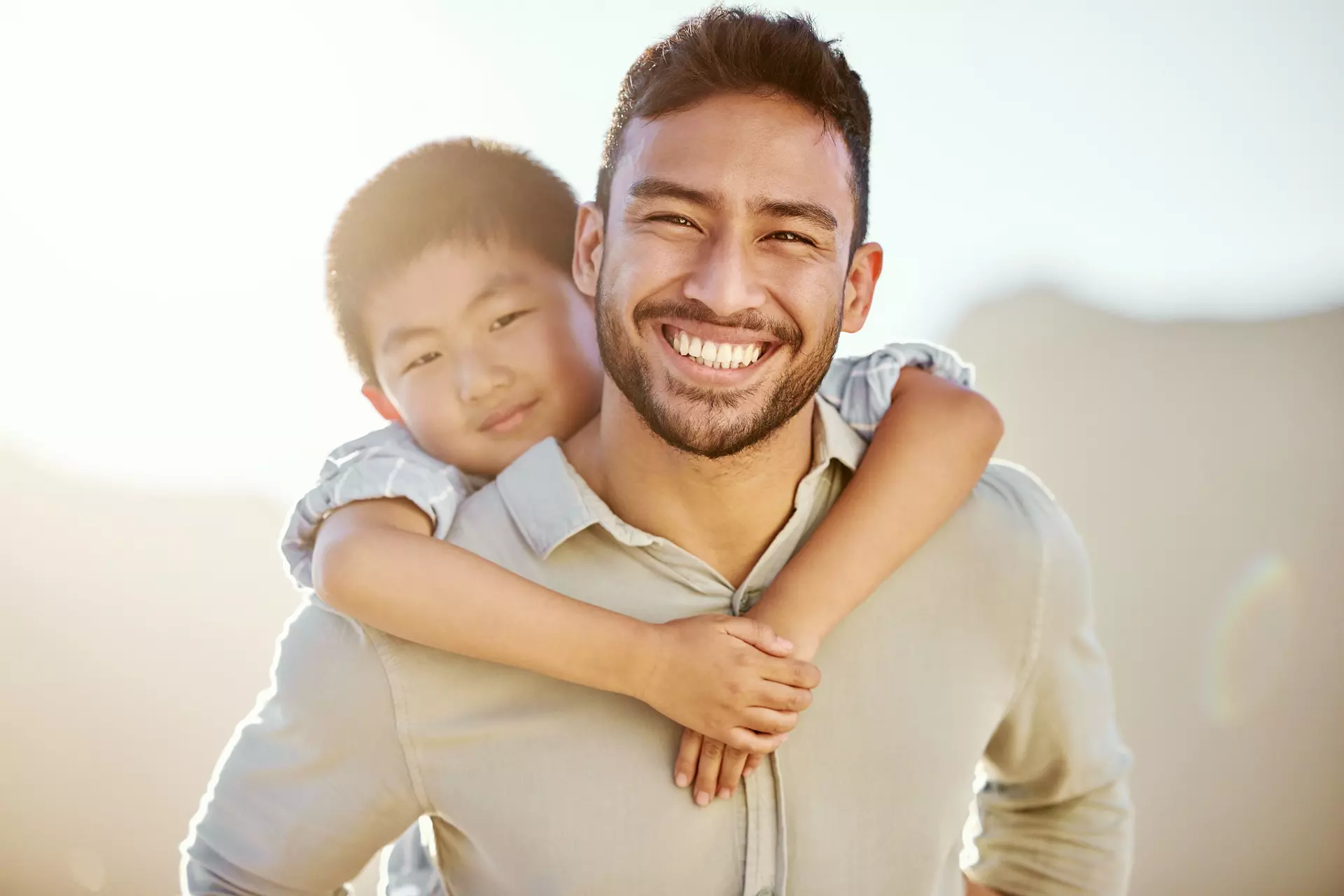 Cropped portrait of a handsome young man piggybacking his son on the beach.