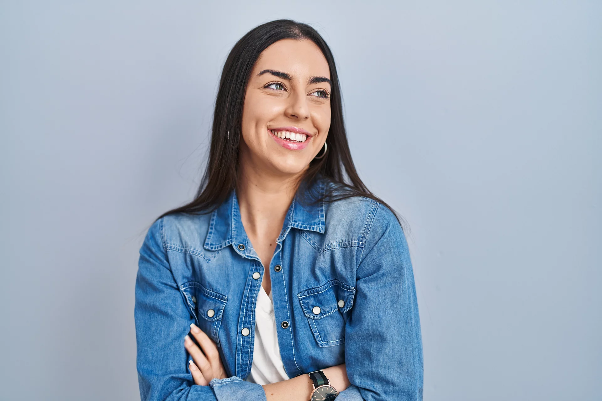 Hispanic woman standing over blue background looking away to side with smile on face, natural expression. laughing confident. 