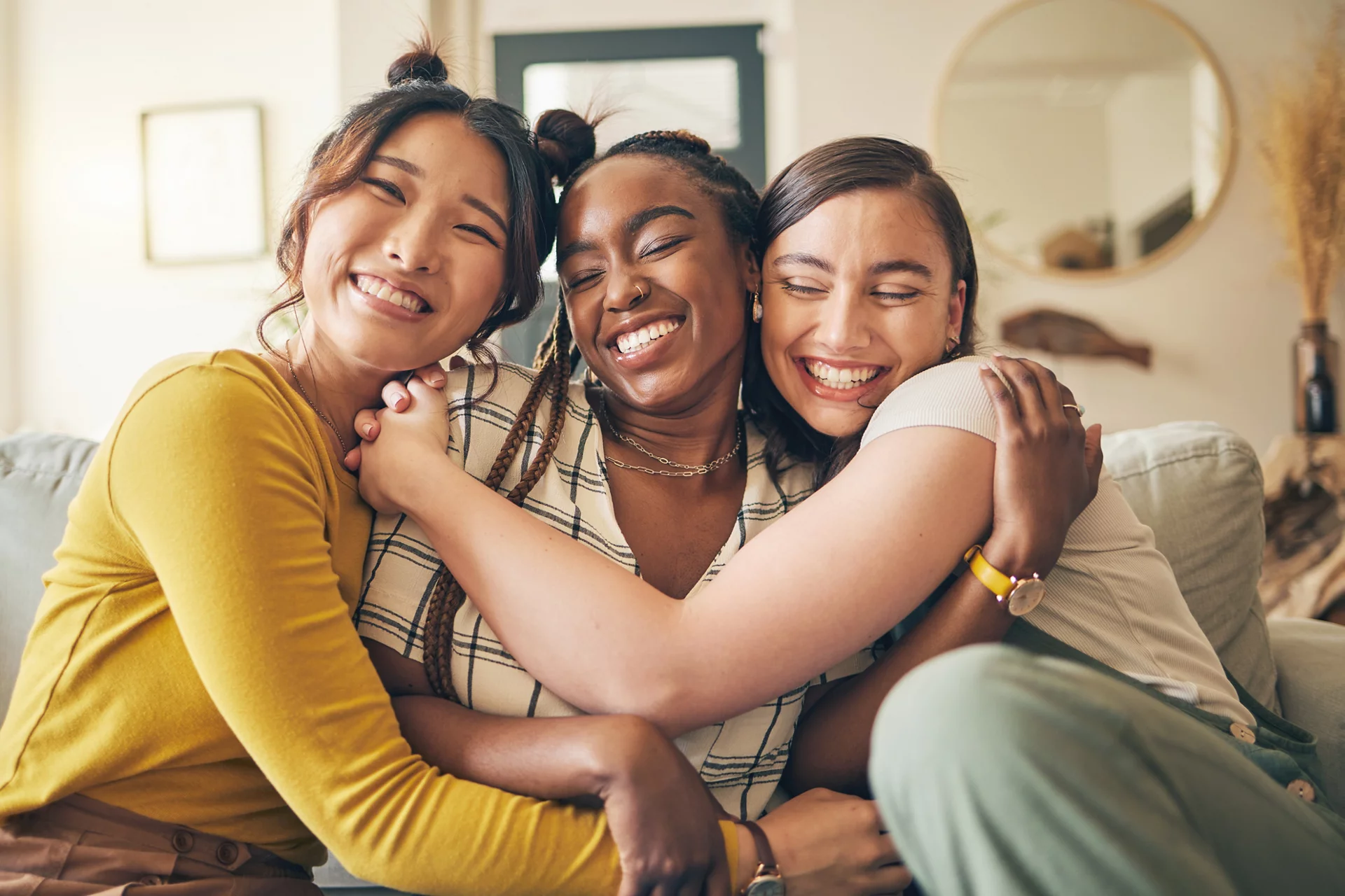 Portrait of a group of women, friends hug on sofa with smile and bonding in living room together in embrace. Hug, love and friendship, girls on couch with diversity, pride and people in home with fun.